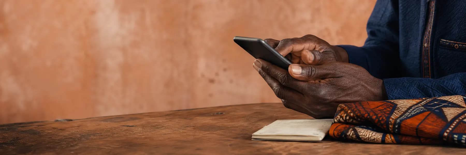 Mains tenant un téléphone sur une table en bois, tissu wax et carnet